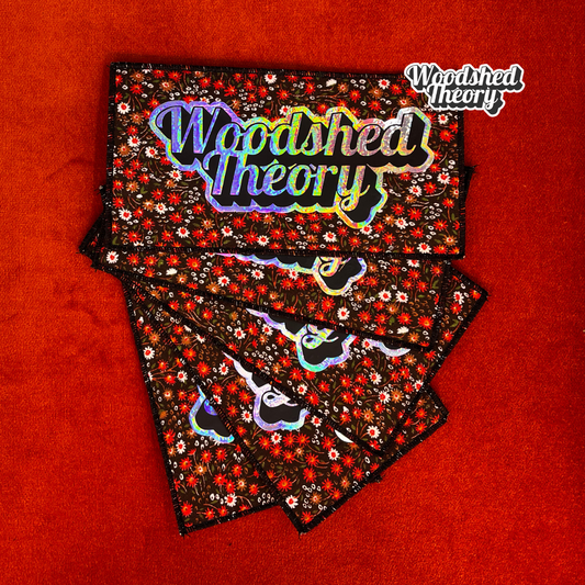 Woodshed Theory logo iron-on patch in holographic script on vintage floral brown canvas background with red and white flowers. group