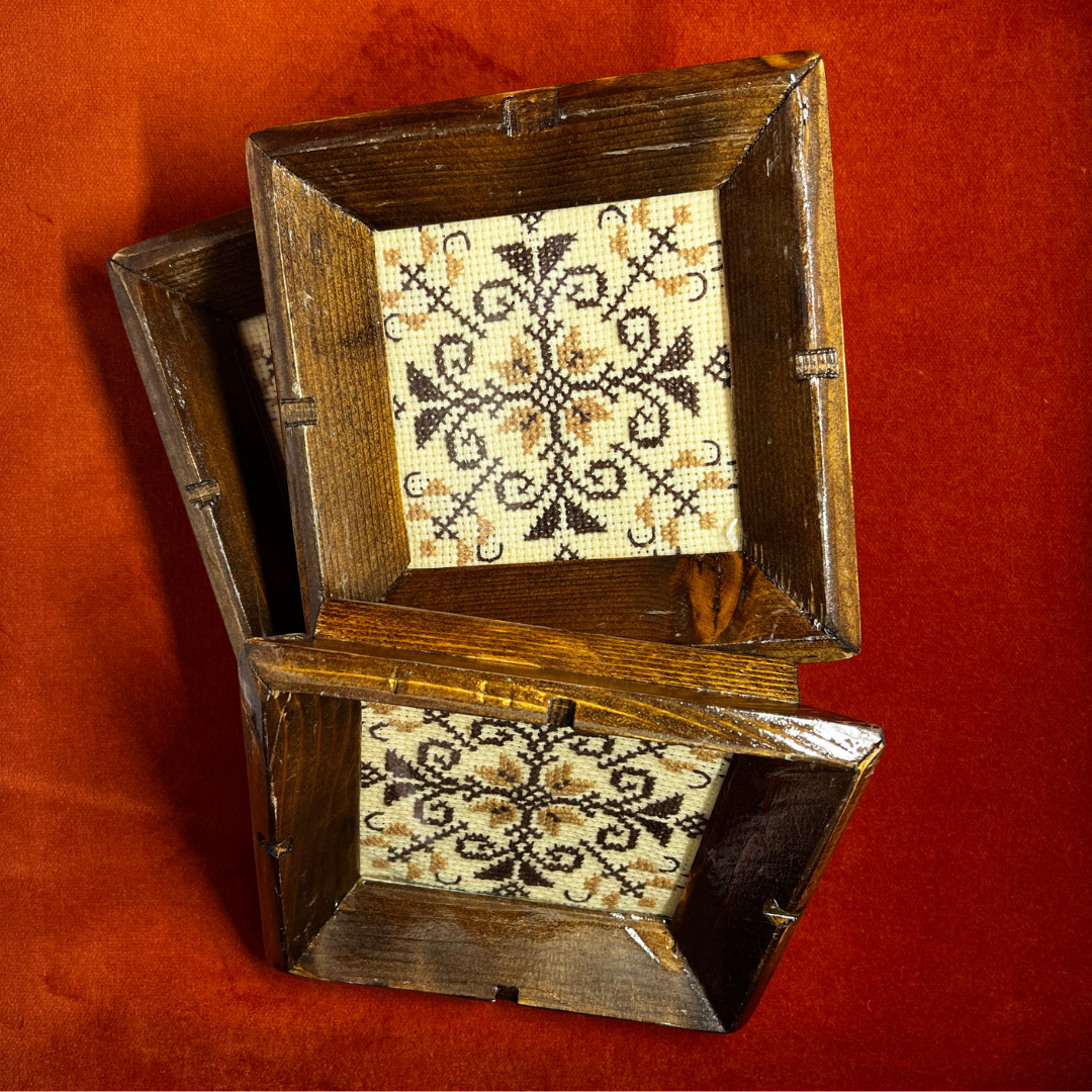 Set of 3 vintage wooden coasters with brown frames, glass covers, and retro cross stitch design in warm tones – perfect for drinks or wall art. top down