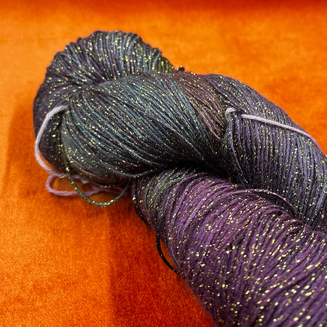 One hank of Blue Heron Rayon Gold Metallic yarn in a blend of purples, greens, and blues with gold shimmer. close up