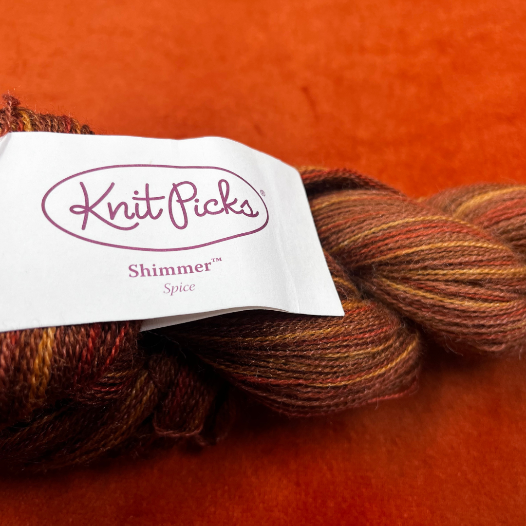 One hank of Knit Picks Shimmer lace weight yarn in a warm Spice color, made of baby alpaca and silk. tag close up