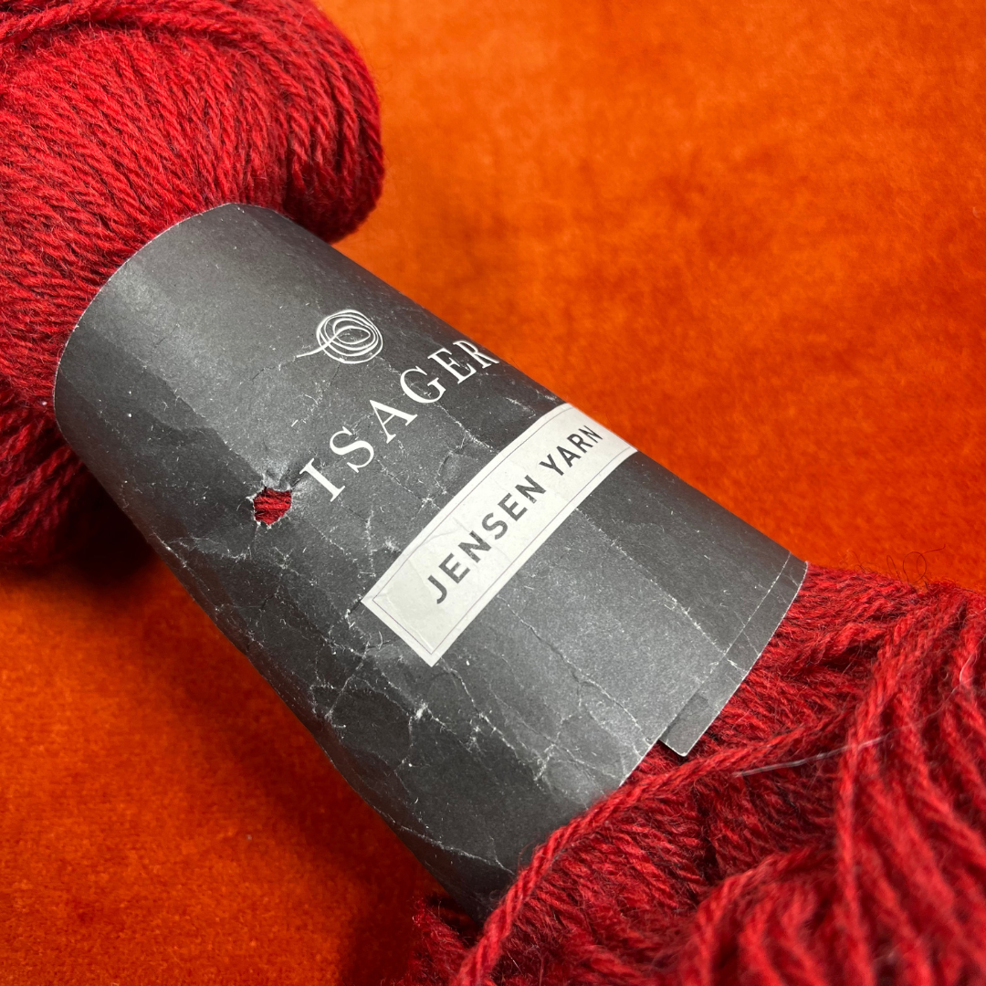 A single hank of Isager Jensen yarn in deep red (32s), 100% wool, neatly twisted and ready for knitting. close up label