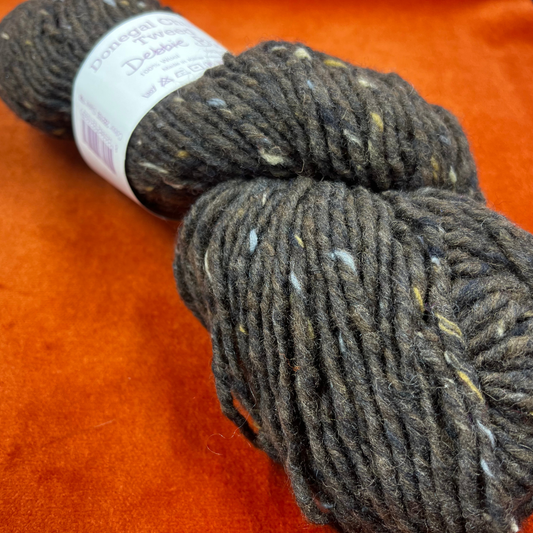 A hank of Debbie Bliss Donegal Chunky Tweed yarn in dark brown with multicolored flecks, 100% wool. close up.