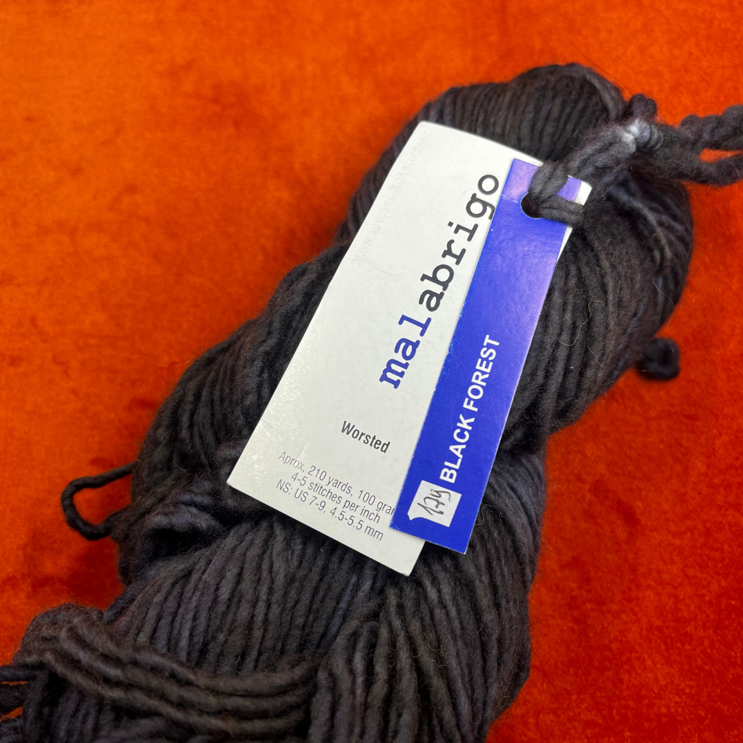 A skein of Malabrigo Worsted Roving in Black Forest, a rich black and dark green tonal yarn made from 100% merino wool. close up tag