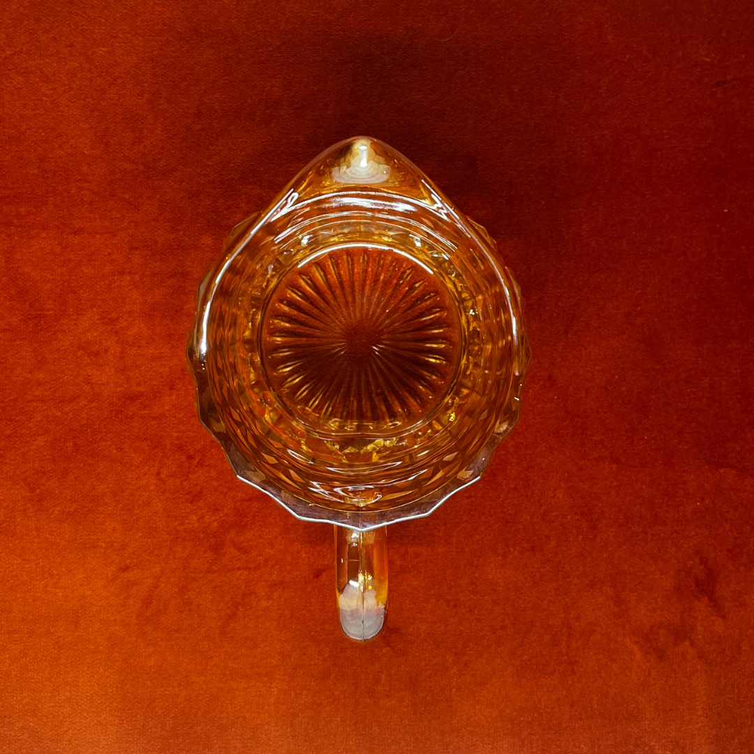 Vintage Jeannette Glass Company Buttons and Bows milk pitcher in iridescent amber, 1947–1949, with handle and shimmering finish. top down