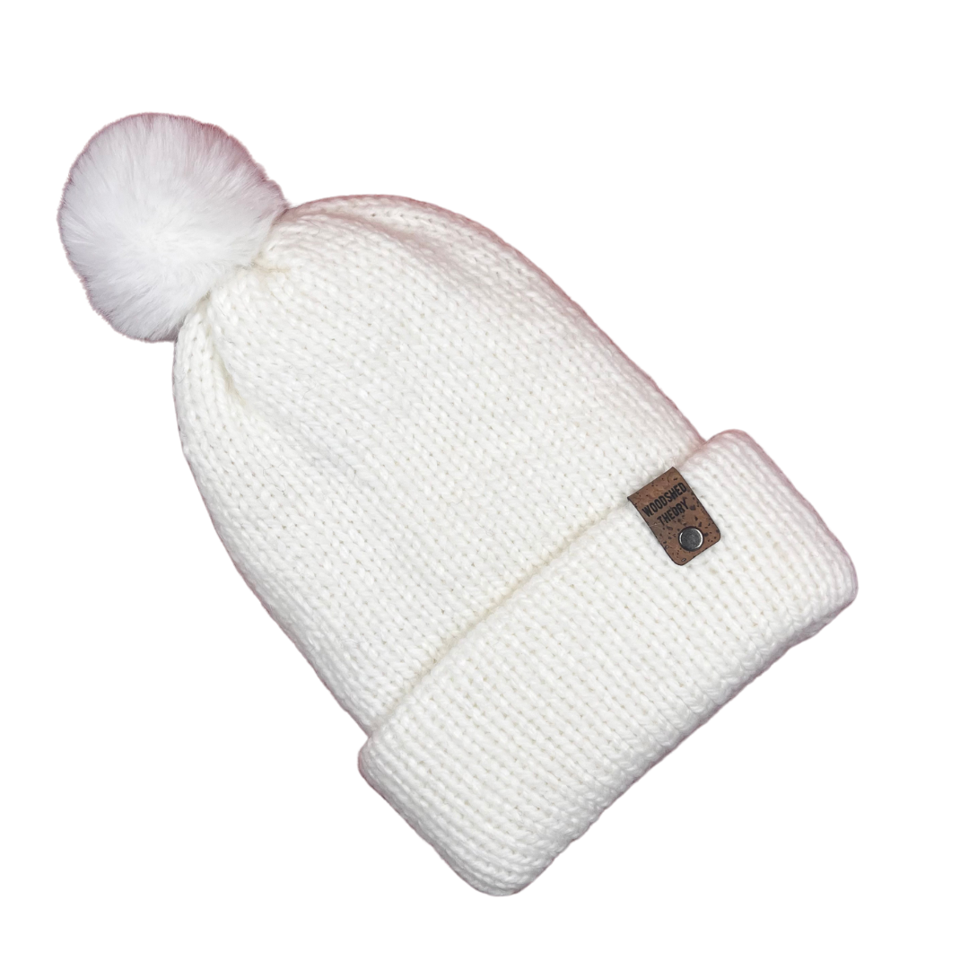 White knit beanie with a pom-pom on a white background alpaca snow beanie in snow hare bright white with custom tag and removable pom pom front flat