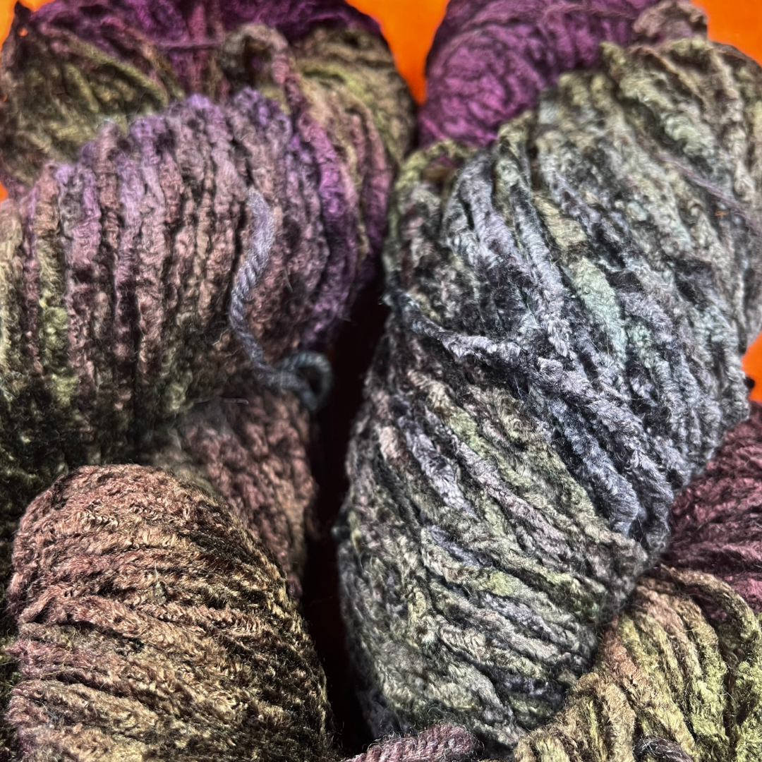 Two hanks of Blue Heron bulky rayon chenille yarn in a variegated blend of purples and greens with a plush, velvety texture. close up