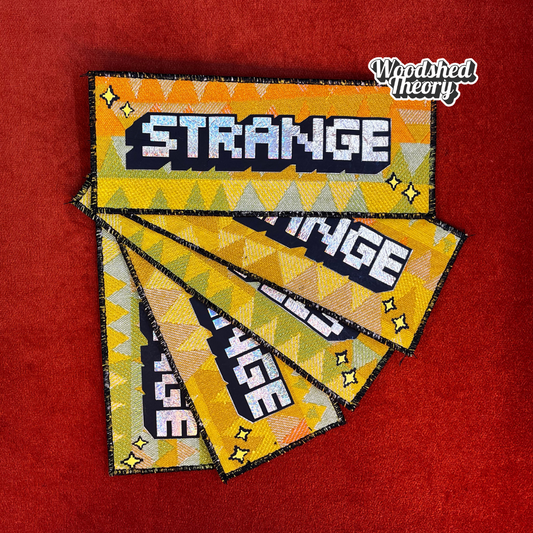 “That’s Strange iron-on patch with holographic pixel font and vintage orange, yellow, and green triangle background – handmade by Woodshed Theory. group