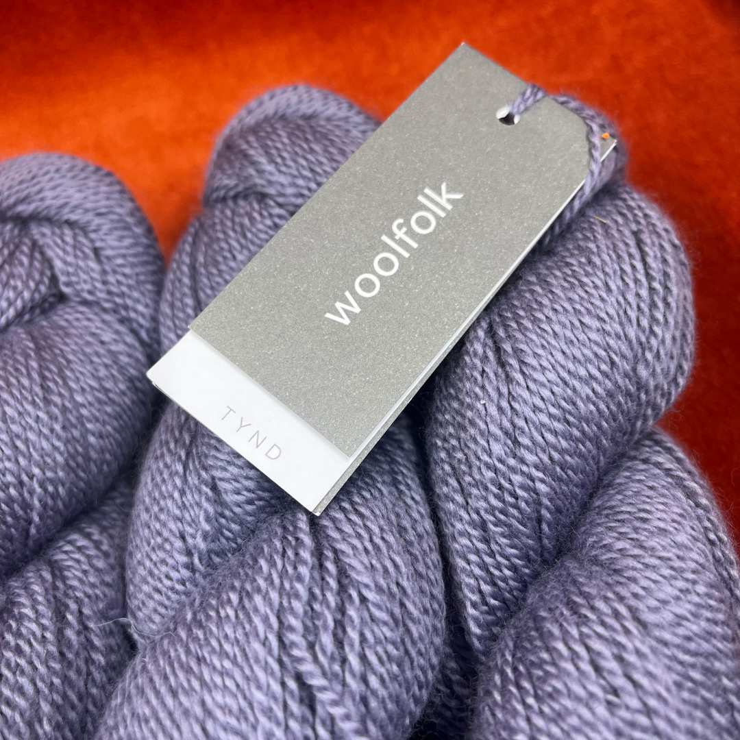Three skeins of Woolfolk TYND yarn in Color 41 (periwinkle grey), fingering weight 100% Ovis 21 Merino wool. close up tag