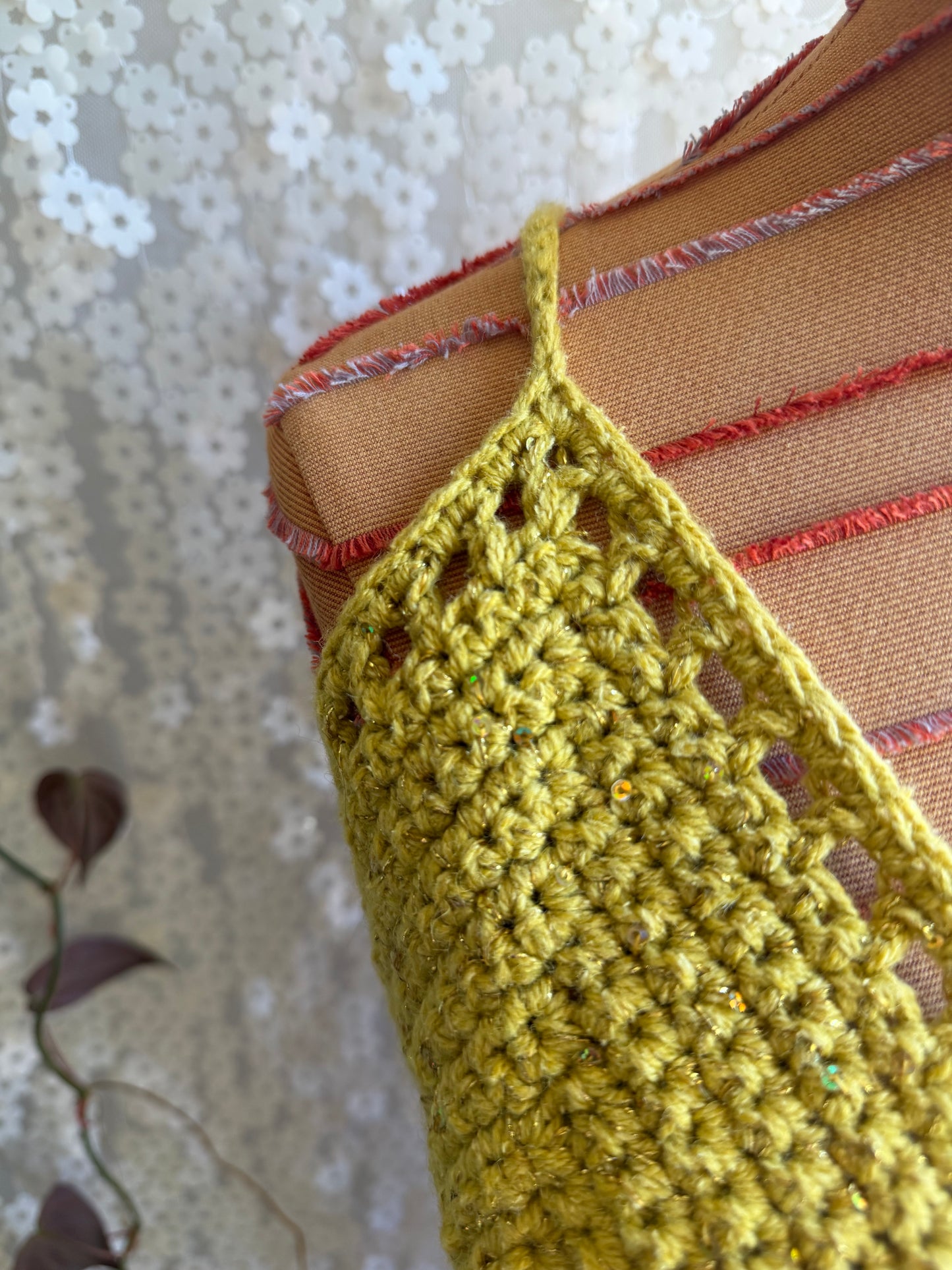 Close-up of a green crochet garment with brown and red accents on a textured background.