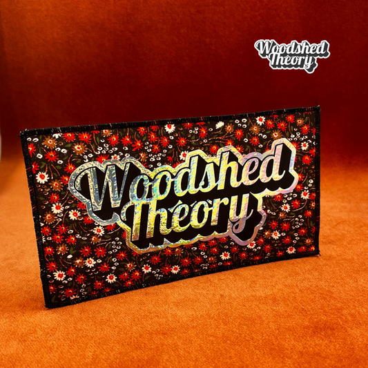 Woodshed Theory logo iron-on patch in holographic script on vintage floral brown canvas background with red and white flowers. front