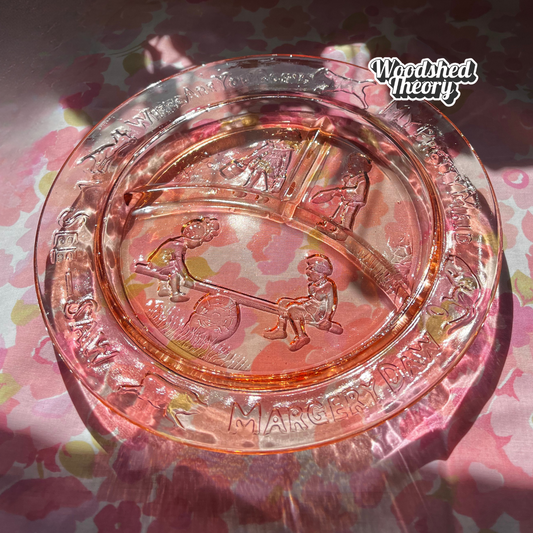 Vintage rose Depression glass children's plate with “Margery Daw” nursery rhyme design and three compartments. Circa 1930s–1940s. front glowing in the sun on pink 