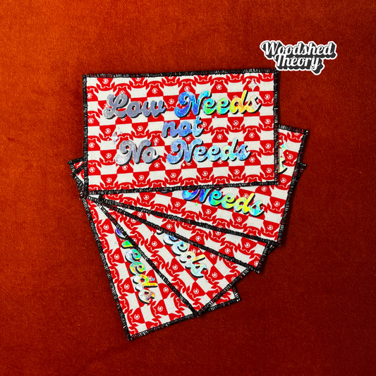Rectangular iron-on patch reading "Low Needs, Not No Needs" in clean bold type. Made with fabric and backing, approx. 5.25 x 3 inches. group of patches halographic red telephone print