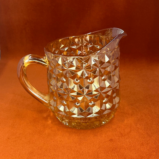 Vintage Jeannette Glass Company Buttons and Bows milk pitcher in iridescent amber, 1947–1949, with handle and shimmering finish. front