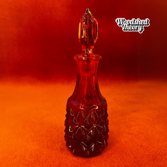 Amberina crystal vial with diamond facets and pointy stopper made in West Germany, glowing under black light front
