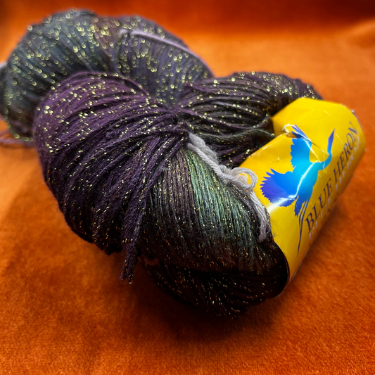 One hank of Blue Heron Rayon Gold Metallic yarn in a blend of purples, greens, and blues with gold shimmer. close up on color