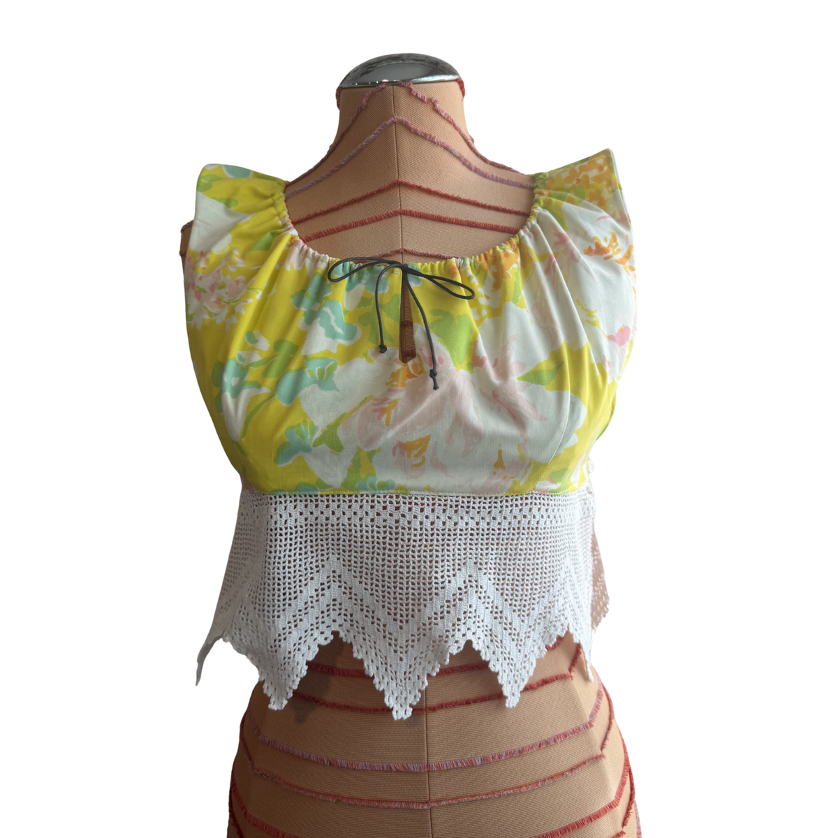 A yellow floral sleeveless blouse with a white crochet hem, displayed on a tan dress form against a white background.
