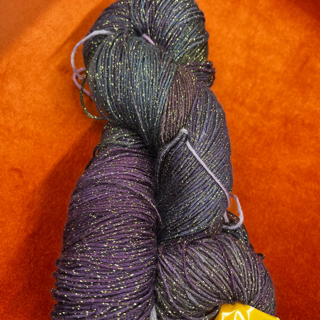 One hank of Blue Heron Rayon Gold Metallic yarn in a blend of purples, greens, and blues with gold shimmer.