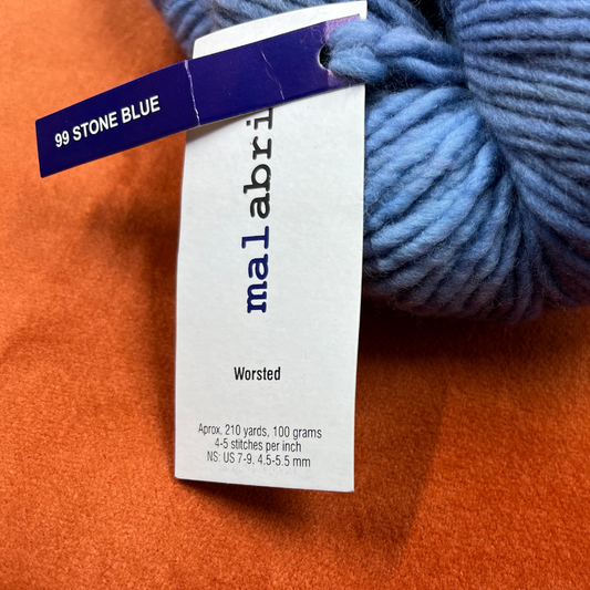 One hank of Malabrigo Worsted Roving in 99 Stone Blue, a soft gray-blue 100% merino wool yarn with subtle tonal variation. close up tag