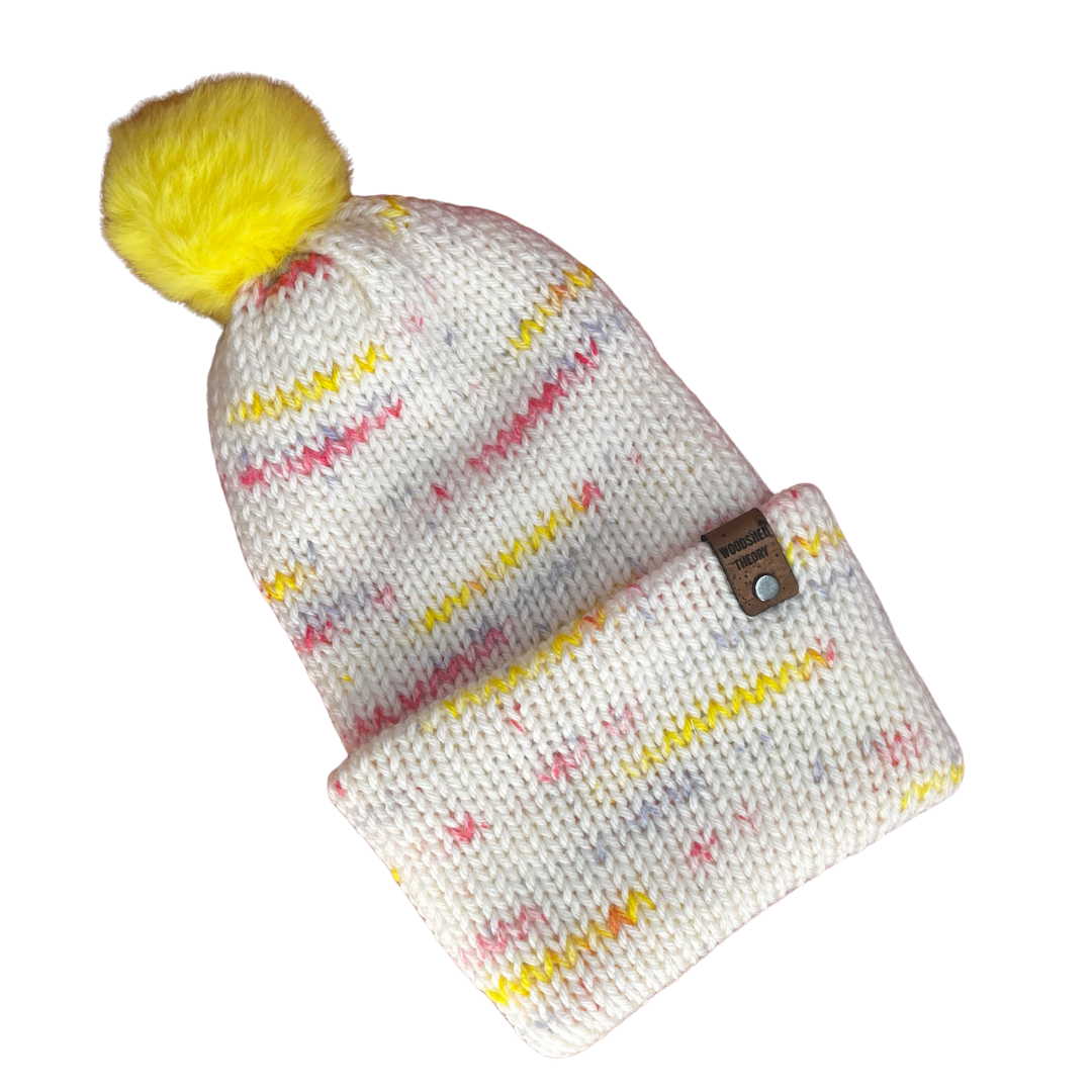 Knitted beanie with colorful pattern and yellow pom-pom on a white background the basic beanie in spring sprinkle