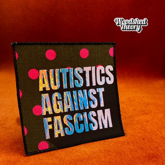 Square iron-on patch with "Autistics Against Fascism" in purple iridescent letters on olive green fabric with pink polka dots. Approx. 4.5 inches square. good trouble front