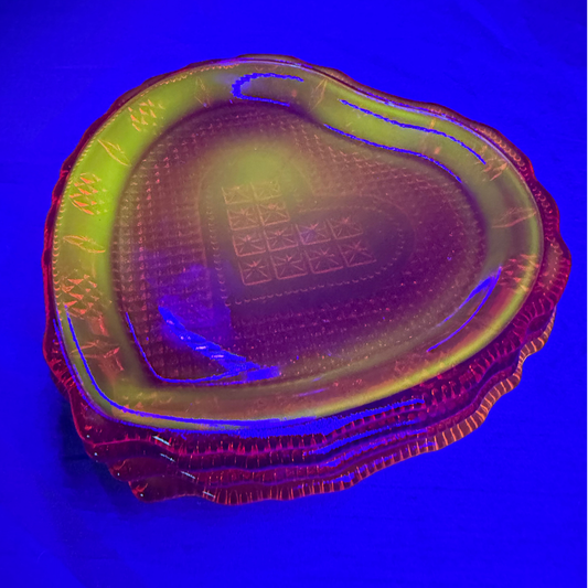 A heart-shaped glass serving platter with a textured pattern and embossed border, shown under blue light that casts a strong blue glow across the translucent surface.