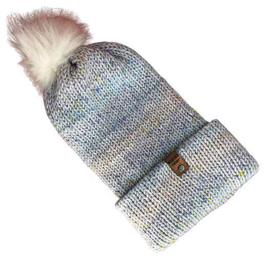 Light blue acrylic knit beanie with multicolor flecks and removable faux fur pom, hand crafted by Woodshed Theory