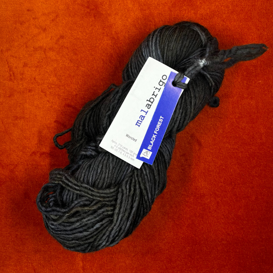 A skein of Malabrigo Worsted Roving in Black Forest, a rich black and dark green tonal yarn made from 100% merino wool. top down