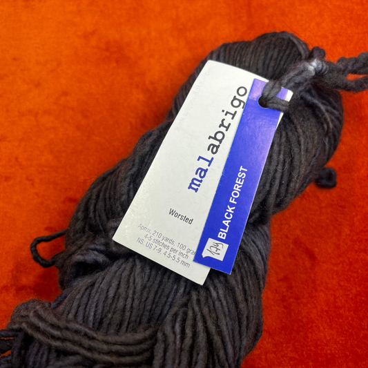 A skein of Malabrigo Worsted Roving in Black Forest, a rich black and dark green tonal yarn made from 100% merino wool. close up tag 