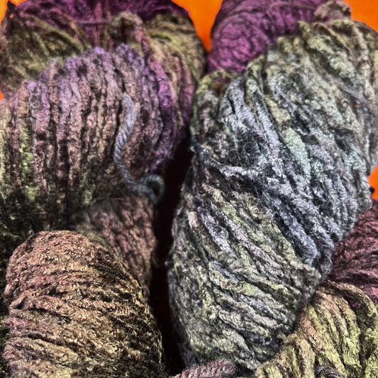 Two hanks of Blue Heron bulky rayon chenille yarn in a variegated blend of purples and greens with a plush, velvety texture. close up