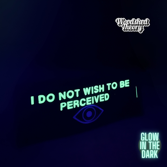 Black iron-on canvas patch with glow-in-the-dark white text reading “I do not wish to be perceived” and a holographic eye illustration. Approx. 3x8 inches. glowing front