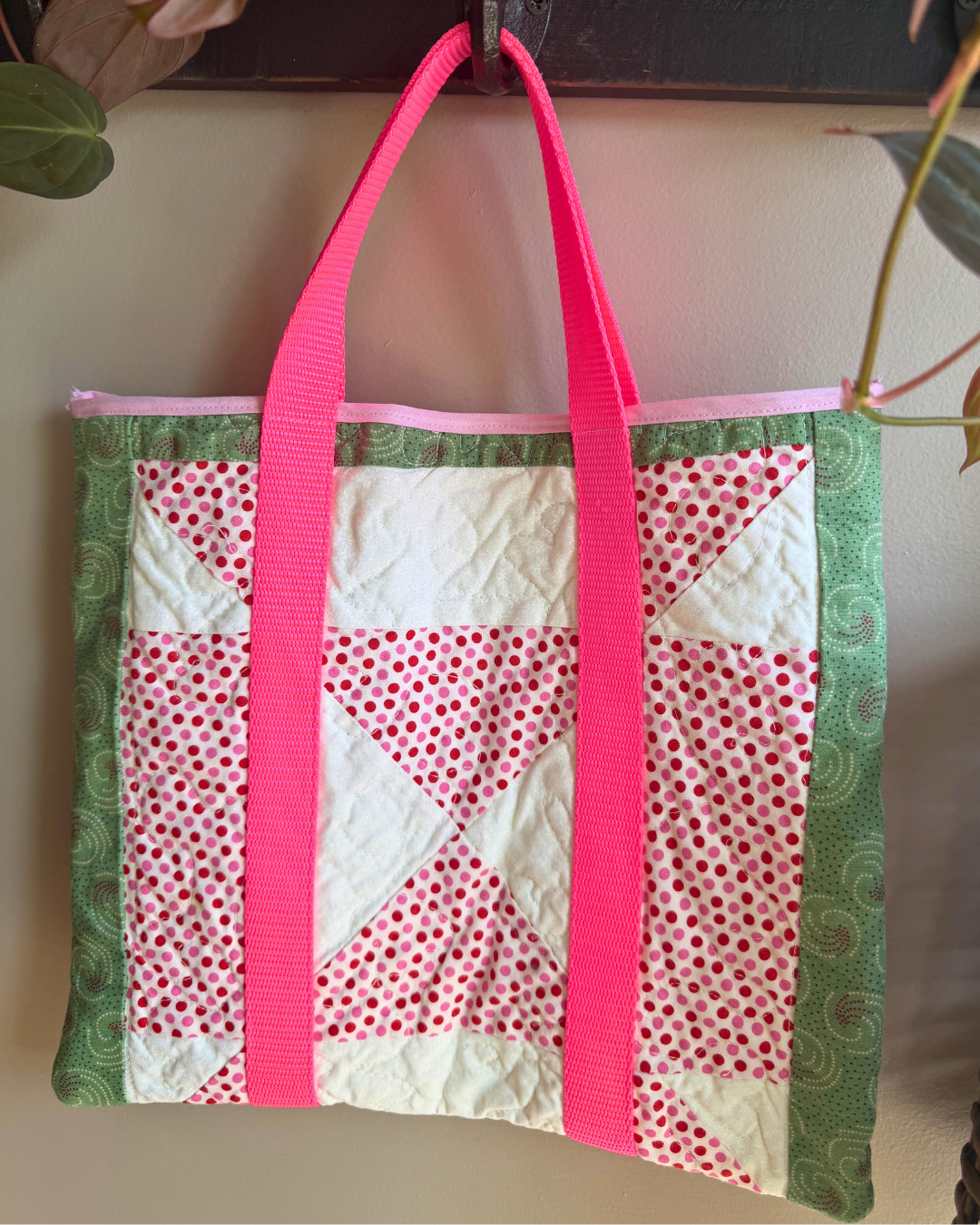 Fabric bag with pink handles and a patchwork pattern on a plain background
