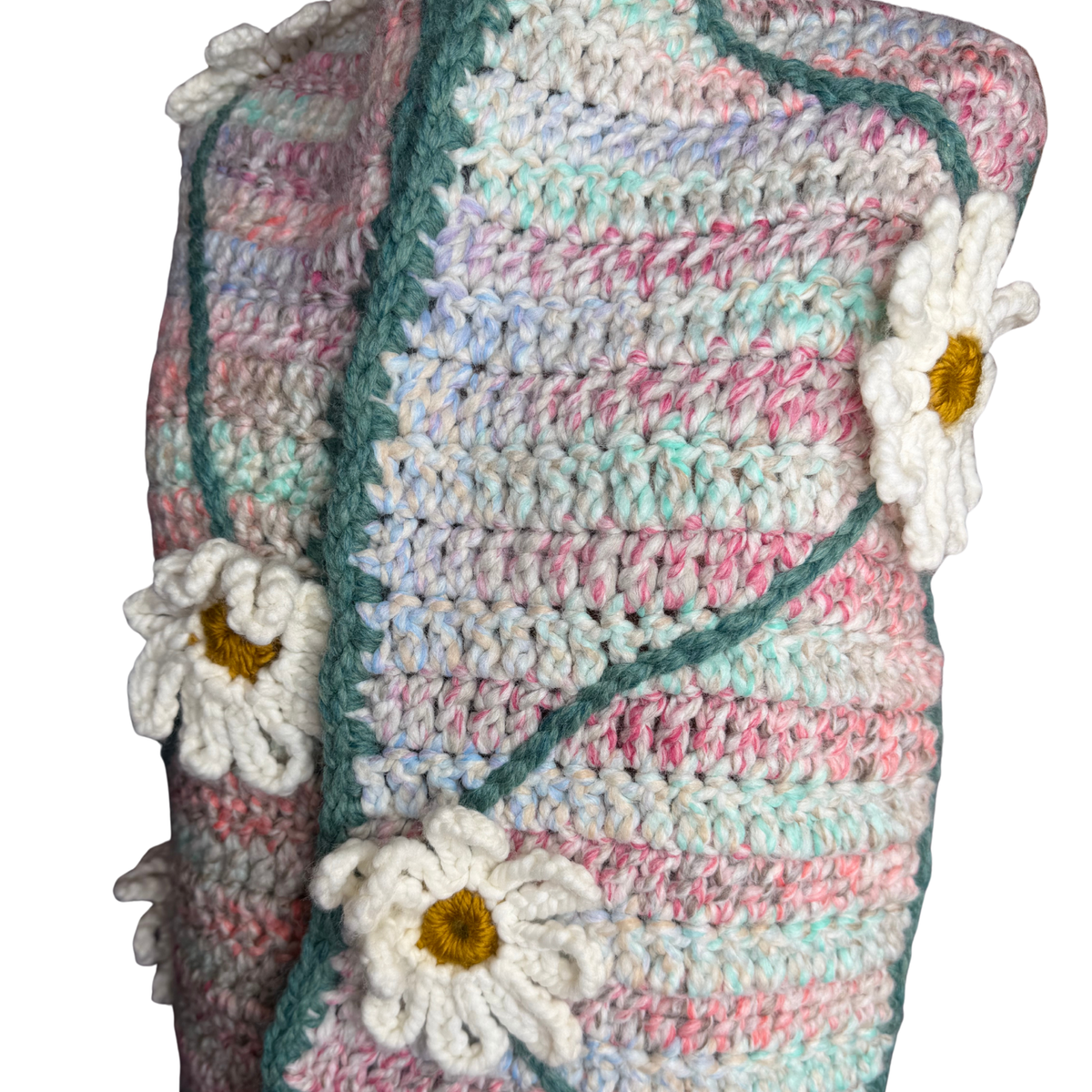 A close-up of a handmade crocheted blanket featuring pastel stripes of pink, mint green, and blue, with white daisy flower appliqués and a teal-green border.