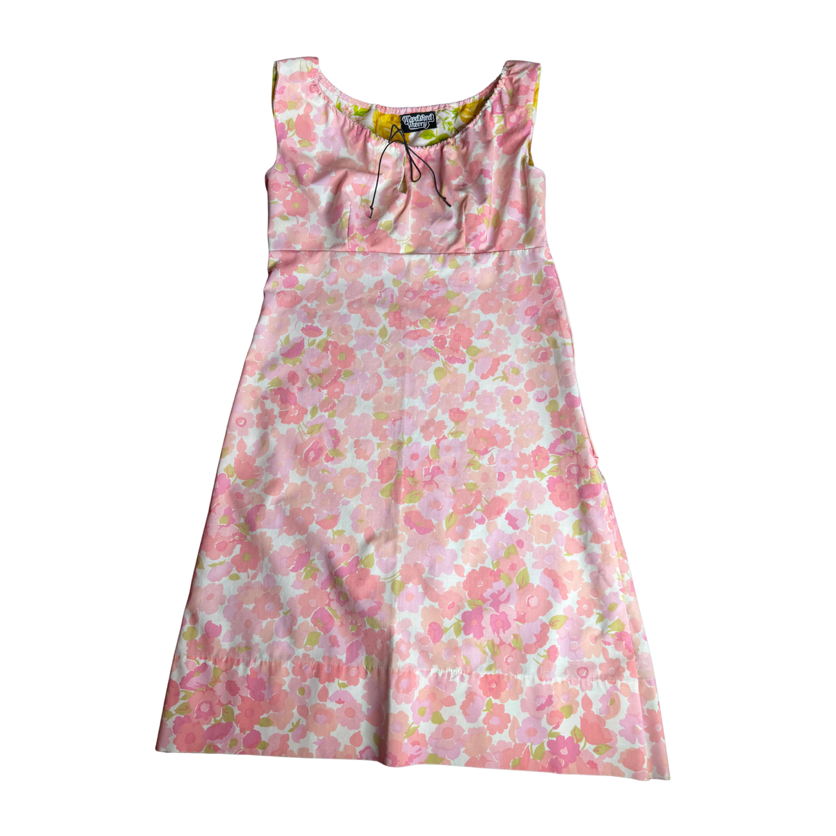 A sleeveless A-line dress with a pink and white floral print, featuring a tie-neck detail and a small black brand label at the inner collar.