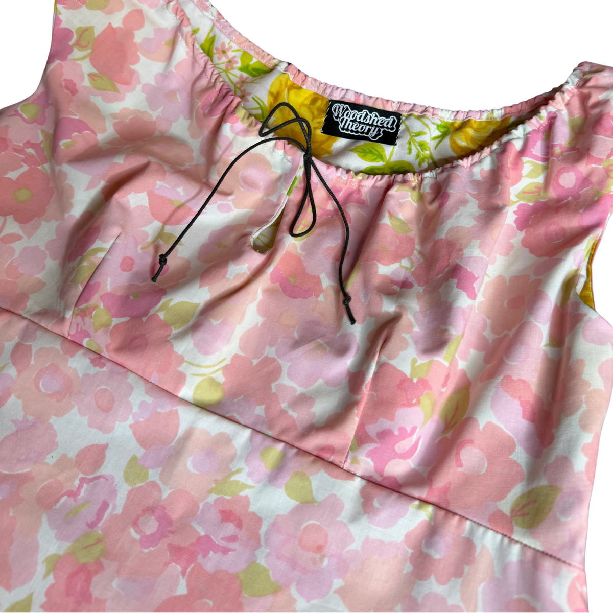 Close-up of a sleeveless top with a pink and white floral print, featuring a black drawstring at the neckline and a visible 'WestStreet Tees' brand label.