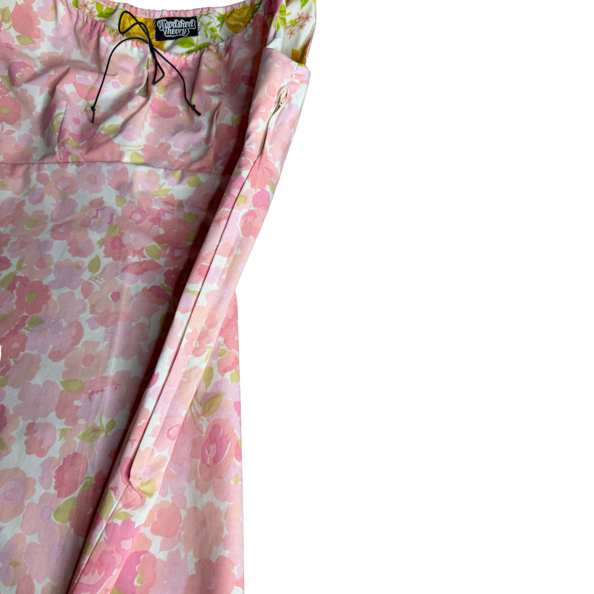 A close-up of a floral print garment, likely a dress or long top, showing the pink and green patterned fabric, black drawstrings, and a visible 'Sandy & Stone' brand label on a plain white background.