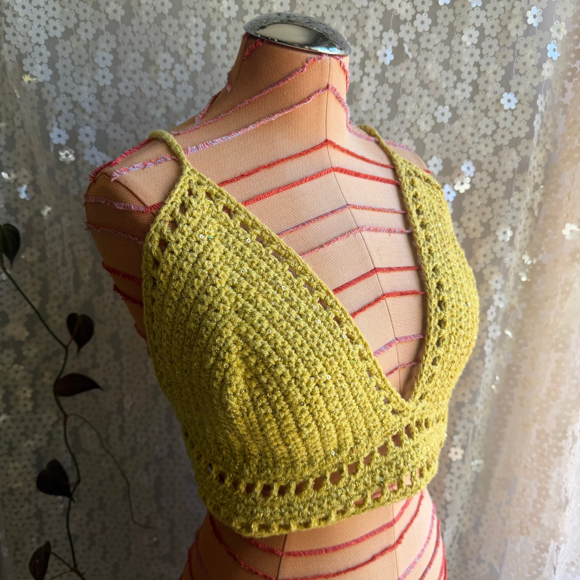 Yellow crochet top on a mannequin against a floral curtain background