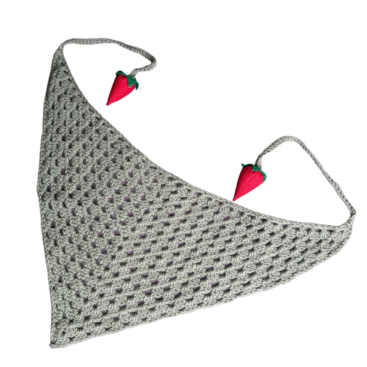 A sage green crochet pet bandana with two small strawberry embellishments on the ties, displayed on a solid white background.