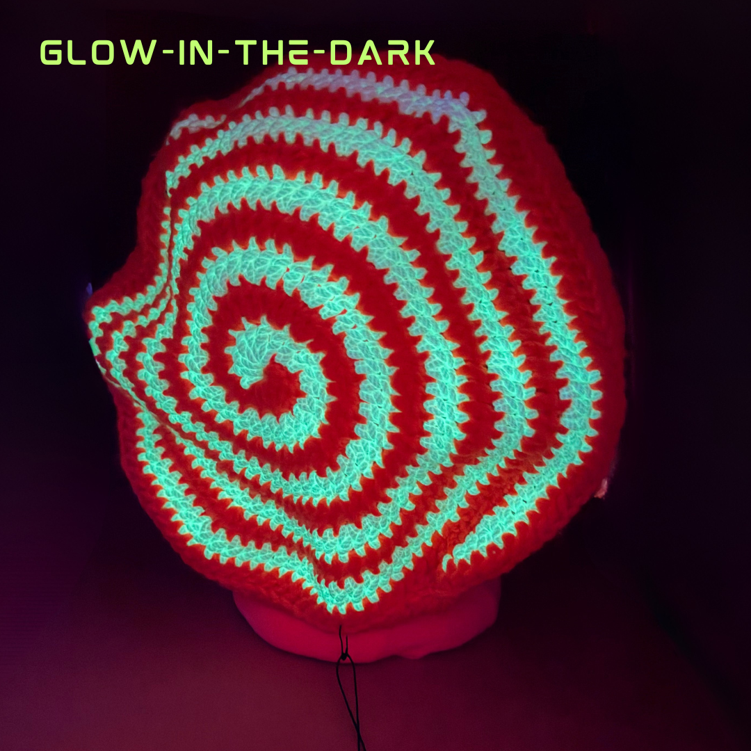A spiral-patterned glow-in-the-dark crochet hat displayed on a mannequin head against a dark background, with the text 'GLOW-IN-THE-DARK' in the top left corner.