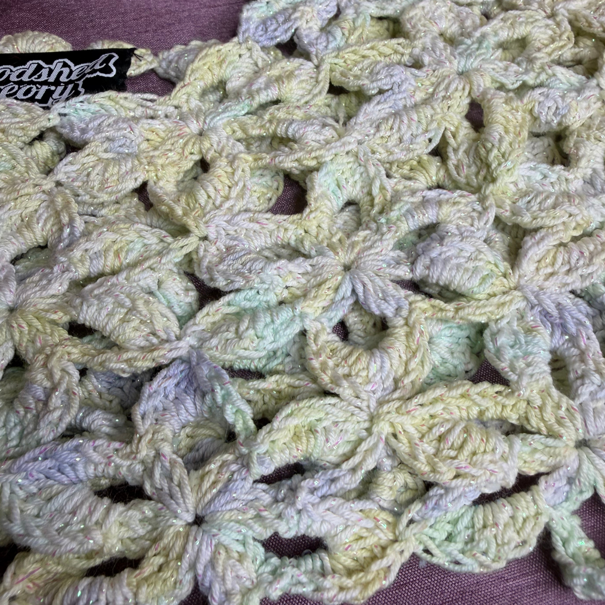A close-up of a handmade crocheted textile featuring textured, multi-colored flower motifs in soft pastel shades of yellow, green, and lavender. A black label with white text reading 'Crafter's Companion' is visible in the upper left corner.