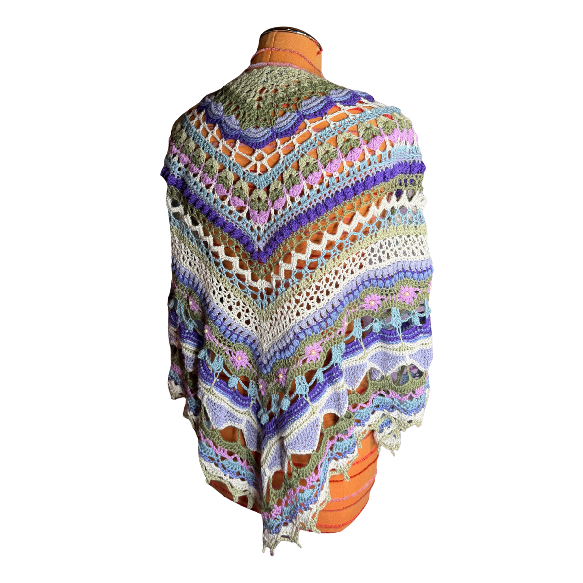 A multicolor crocheted shawl with intricate lace patterns and a scalloped fringe, draped over an orange mannequin torso against a white background.