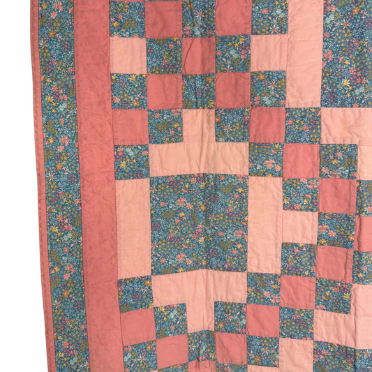 A close-up of a quilted textile with a patchwork design featuring dusty pink, coral, and teal floral fabrics.