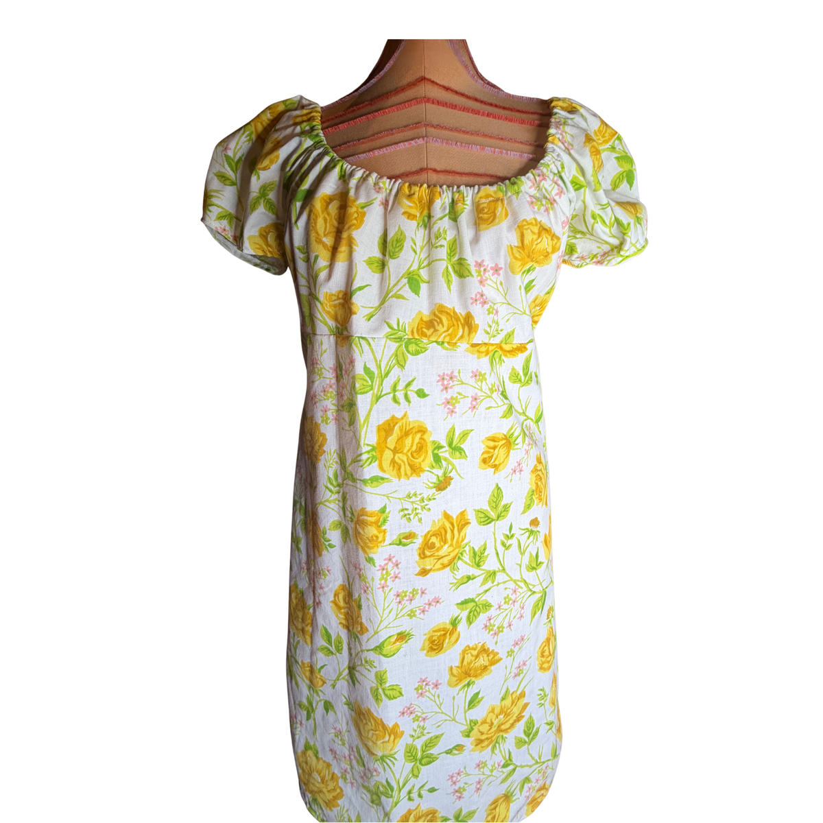 A short-sleeve white dress with a yellow rose and green leaf floral print, displayed on a wooden dress form against a white background.